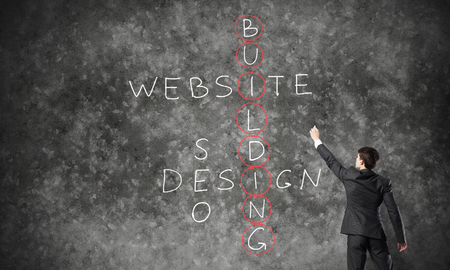 Businessman standing with back and drawing crossword on blackboardの写真素材