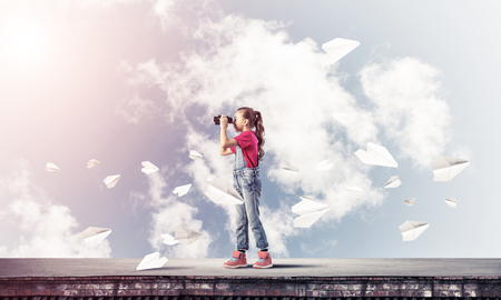 Cute girl of school age on building roof looking in binocularsの写真素材
