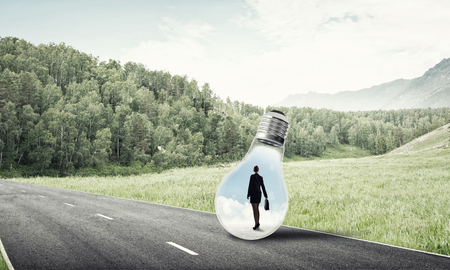 Young businesswoman trapped inside of light bulb on asphalt roadの写真素材