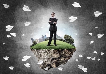 Elegant confident businessman standing on green floating island against concrete backgroundの写真素材