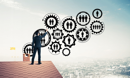 Young man standing with back on roof and drawing gear teamwork concept. Mixed mediaの写真素材