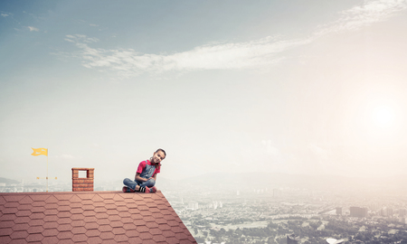 Cute kid girl sitting on brick house roof and looking fearlessly downの写真素材
