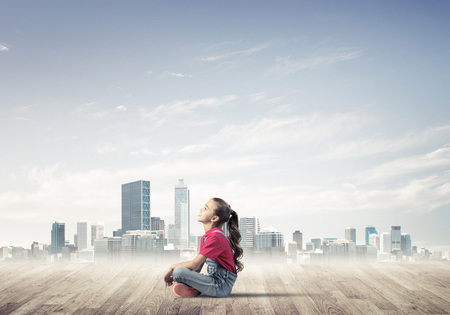 Cute kid girl sitting on wooden floor and looking upの写真素材