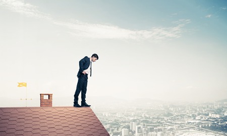 Young businessman standing on edge of house brick roof and looking down. Mixed mediaの写真素材
