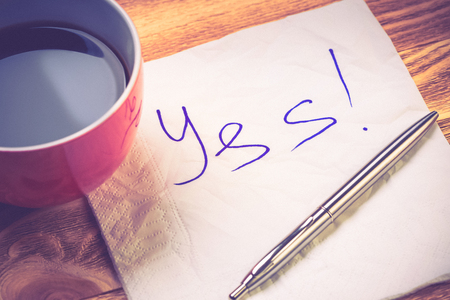 Coffee cup pen and napkin with words on wooden tableの写真素材