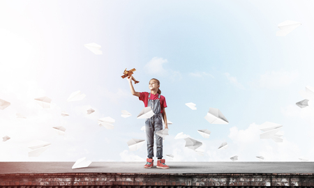 Cute happy kid girl on building top playing with retro plane modelの写真素材