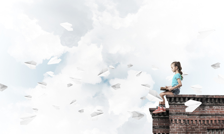 Cute kid girl sitting on building roof and reading bookの写真素材