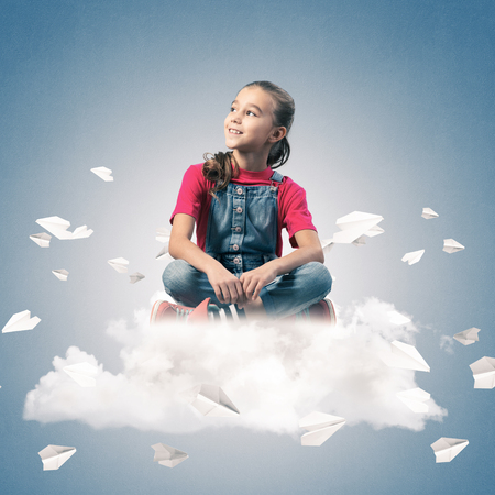 Cute kid girl sitting on cloud and paper planes flying aroundの写真素材