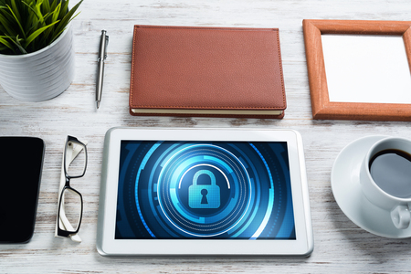 Business workplace with office stuff and tablet with padlock icons on screenの写真素材