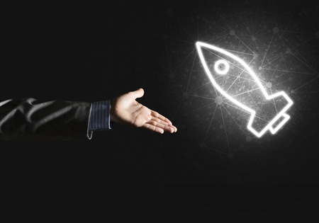 Rocket glowing icon and businessman hand on dark background