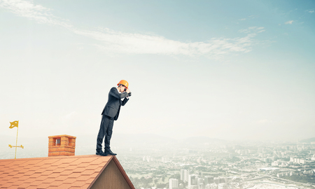 Young businessman in suit and helmet on roof edge in search of something new. Mixed mediaの写真素材