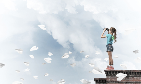 Cute girl of school age on building roof looking in binocularsの写真素材