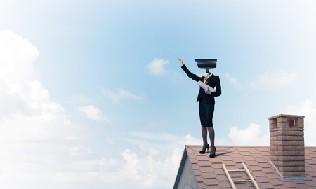 Faceless businesswoman with camera zoom instead of head standing on house roofの写真素材