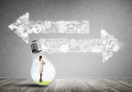 Businesswoman inside of light bulb in empty concrete roomの写真素材