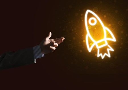 Rocket glowing icon and businessman hand on dark backgroundの写真素材