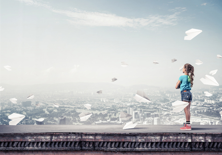Cute kid girl standing on building roof and paper planes flying aroundの写真素材