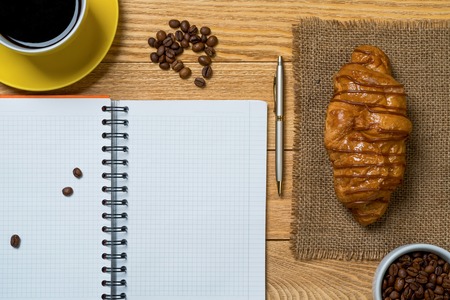 Opened notepad and cup of coffee with donut on wooden tableの写真素材