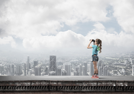 Cute girl of school age on building roof looking in binocularsの写真素材
