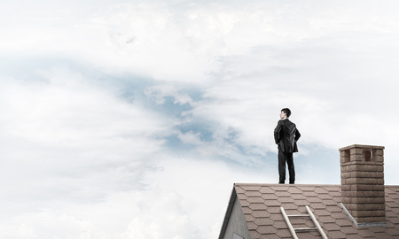 Young determined businessman standing with back on house roof and looking away. Mixed mediaの写真素材