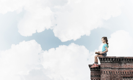 Cute kid girl sitting on building roof and reading bookの写真素材