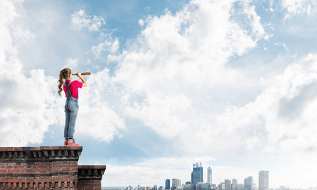 Cute kid girl standing on house roof and looking in spyglassの写真素材