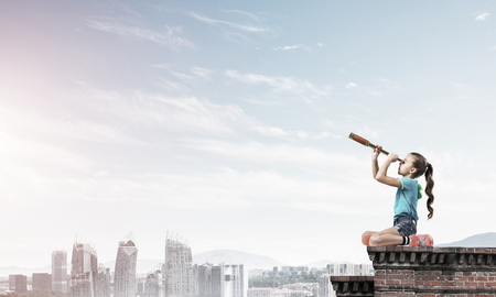 Cute kid girl sitting on house roof and looking in spyglassの写真素材