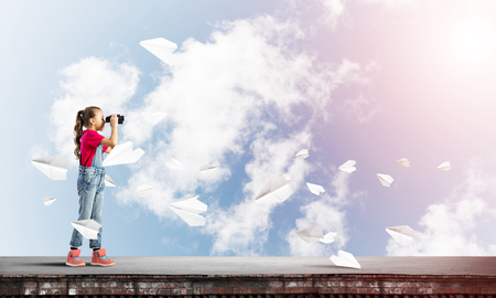 Cute girl of school age on building roof looking in binocularsの写真素材