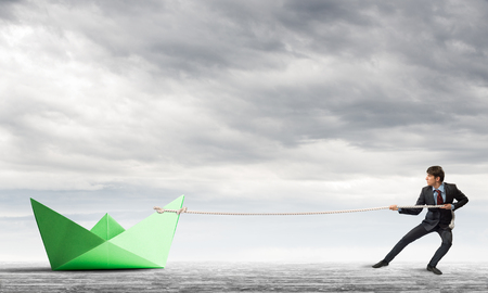 Successful businessman pulling with rope paper boatの写真素材