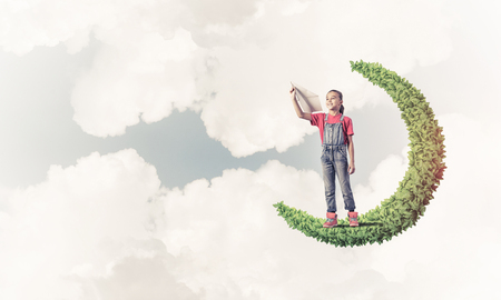 Cute kid girl standing on green moon playing with airplane toyの写真素材
