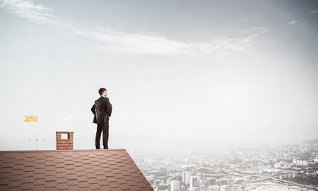 Young determined businessman standing on house roof and looking away. Mixed mediaの写真素材
