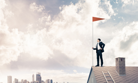 Businessman standing on house roof and red holding flag. Mixed mediaの写真素材