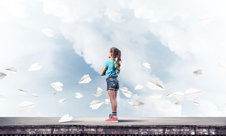 Cute kid girl standing on building roof and paper planes flying aroundの写真素材