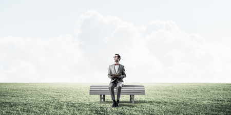 Funny man in red glasses and suit sitting on bench and reading bookの写真素材