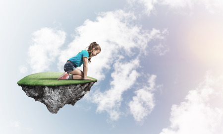Cute smiling girl sitting on floating island high in skyの写真素材