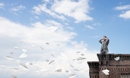 Frustrated businessman sitting on roof and closing ears with handsの写真素材