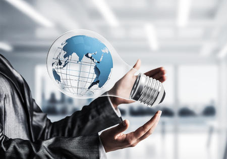 Closeup of business woman in suit holding in hands lightbulb with Earth globe inside with office view background.の写真素材