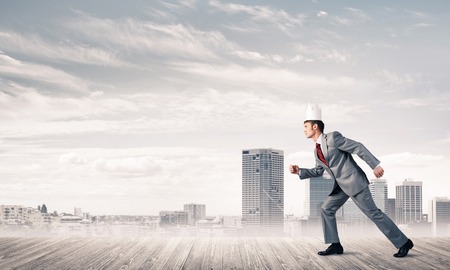 Young handsome businessman wearing white paper crown running in a hurryの写真素材