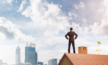 Young determined businessman standing on house roof and looking away. Mixed mediaの写真素材