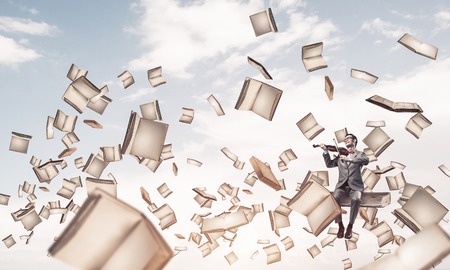 Young man wearing suit and glasses floating in sky and playing violinの写真素材
