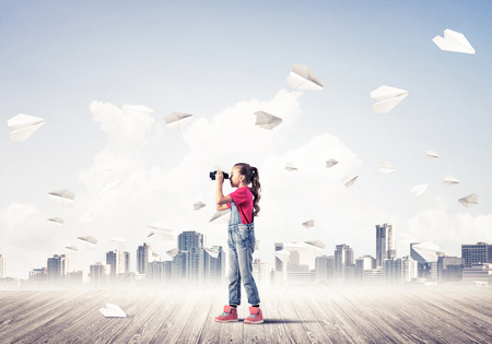 Cute kid girl stand on wooden floor and paper planes flying aroundの写真素材