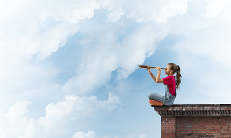 Cute kid girl sitting on house roof and looking in spyglassの写真素材
