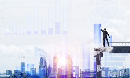 Businessman in suit drawing graphs on modern statistical media interface while standing on broken bridge with cityscape and sunlight on background. 3D rendering.の写真素材