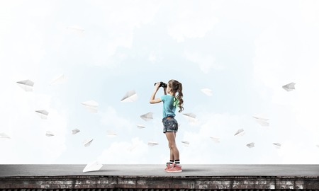 Cute girl of school age on building roof looking in binocularsの写真素材