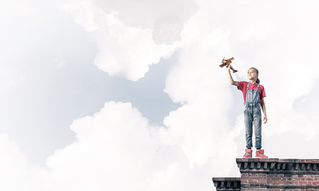 Cute happy kid girl on building top playing with retro plane modelの写真素材