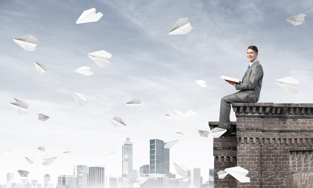 Young businessman sitting on building top with red book in handsの写真素材
