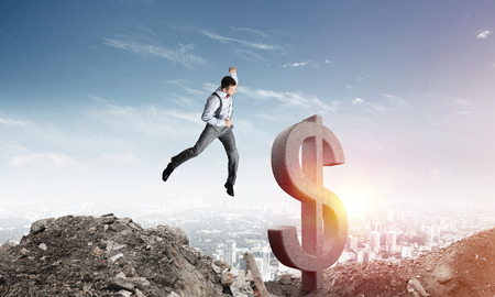 Jumping businessman in smart casual wear crashing big dollar symbol with city view on background.の写真素材