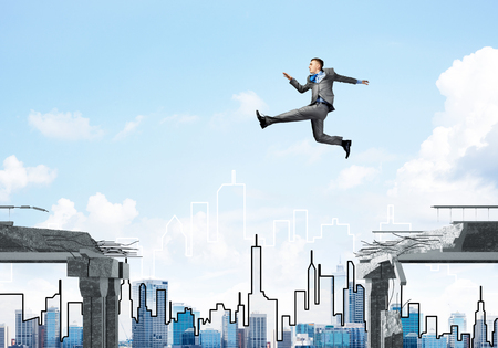 Businessman jumping over gap in concrete bridge as symbol of overcoming challenges. Cityscape on background. 3D rendering.の写真素材