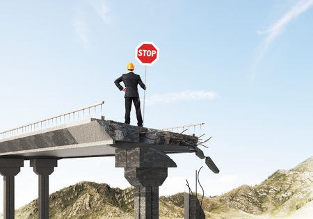 Rear view of engineer in helmet holding stop sign while standing on broken bridge with skyscape and nature view on background. 3D rendering.の写真素材