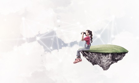 Cute girl on floating island looking in spyglass presenting social connection conceptの写真素材
