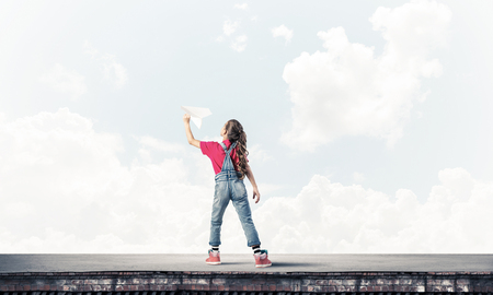 Cute happy kid girl on building top playing with paper planeの写真素材